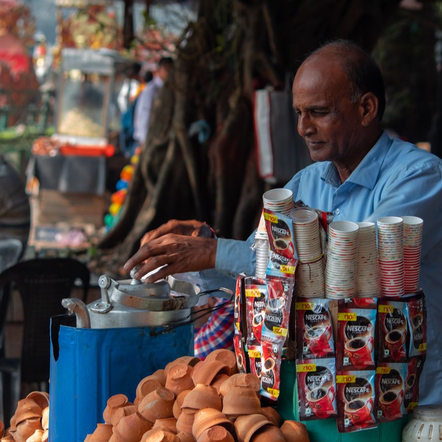 A chai vendor pouring cutting chai for customers at his stall
